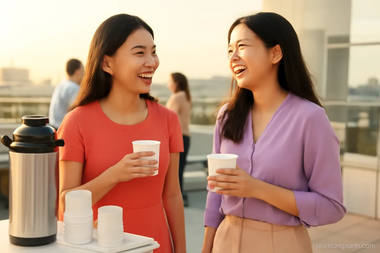 Eye-level medium shot of two young Vietnamese women chatting and laughing beside a coffee station at a bright rooftop networking event, holding paper cups, warm sunset light, coral and lilac tones