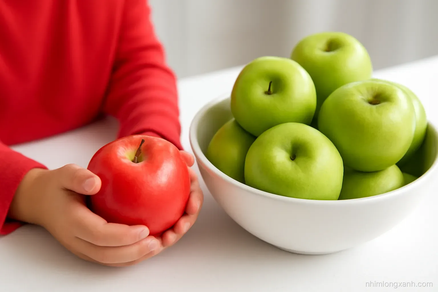 Close-up macro of a Vietnamese child small hands holding one red apple next to a bowl of many green apples on a white kitchen counter, crisp daylight, red and fresh green palette