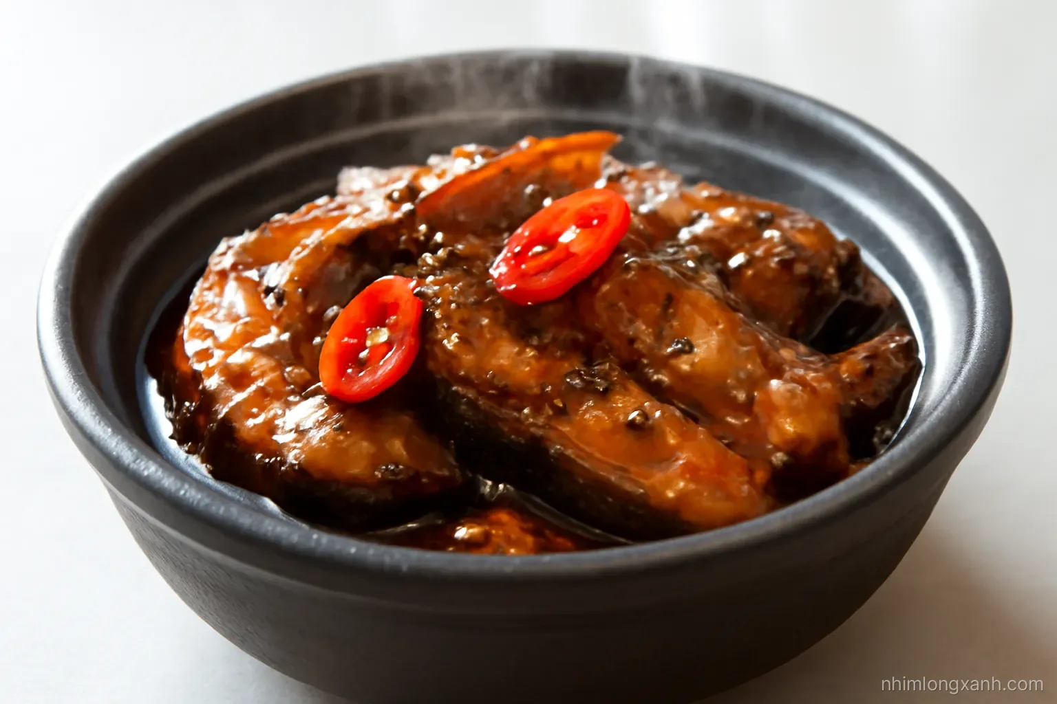 Close-up macro of a dark clay pot with thick slices of braised snakehead fish in shiny brown sauce, sliced red chili and black pepper, steam rising, dramatic side light