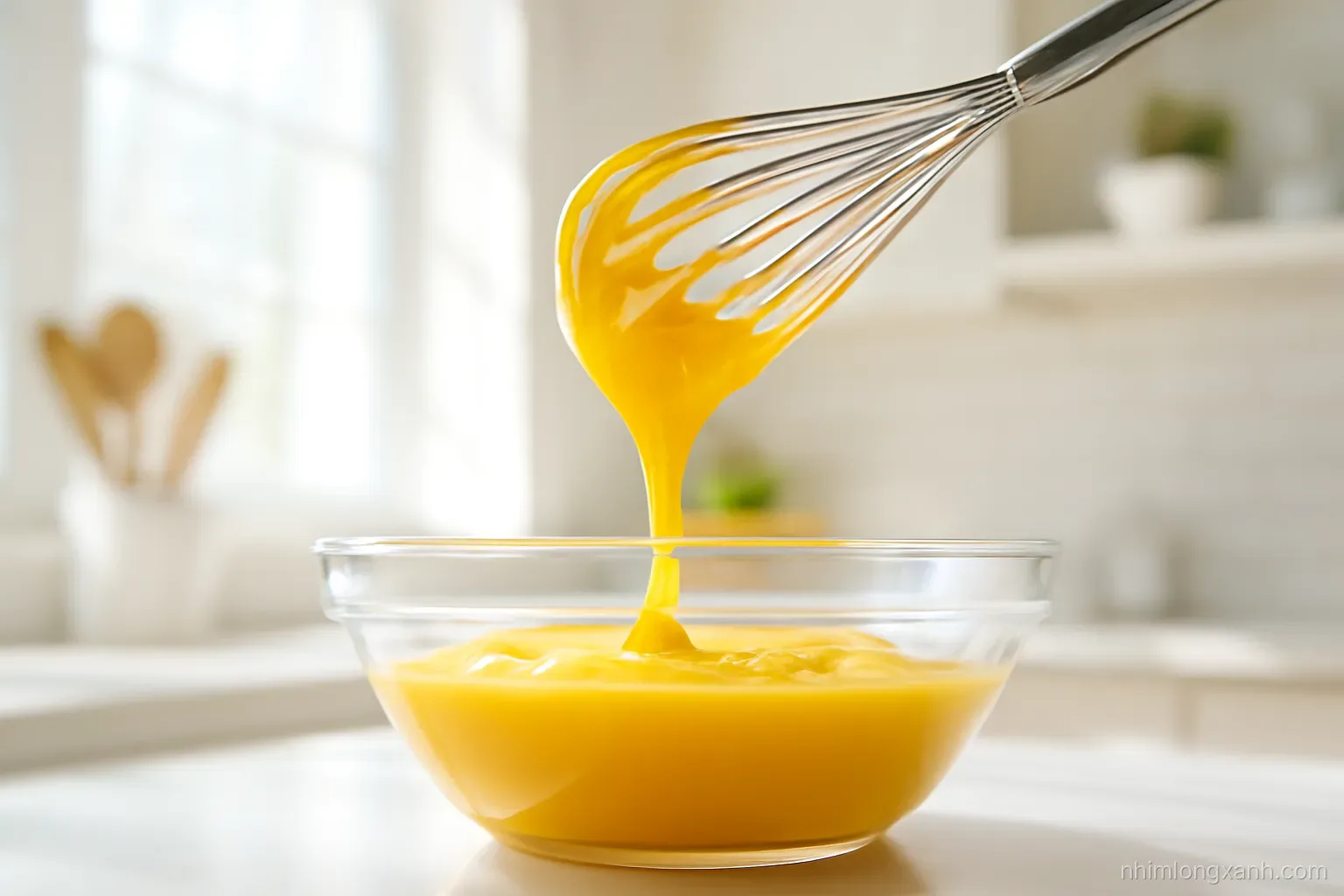 Low angle close-up of a whisk lifting thick golden egg yolk spread from a glass bowl, thin stream of oil pouring in, sunny yellow and white tones, bright kitchen backdrop
