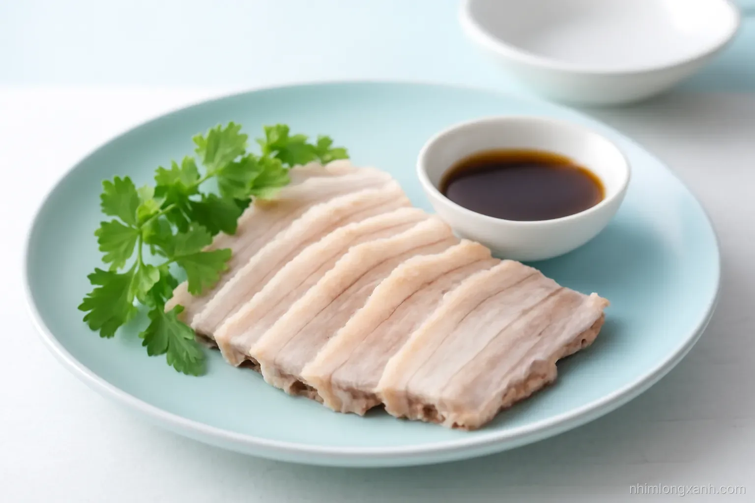 Side angle close-up of thin slices of boiled pork belly fanned on a pale blue ceramic plate with herbs and a small dipping bowl, cool daylight, crisp white and sky blue palette