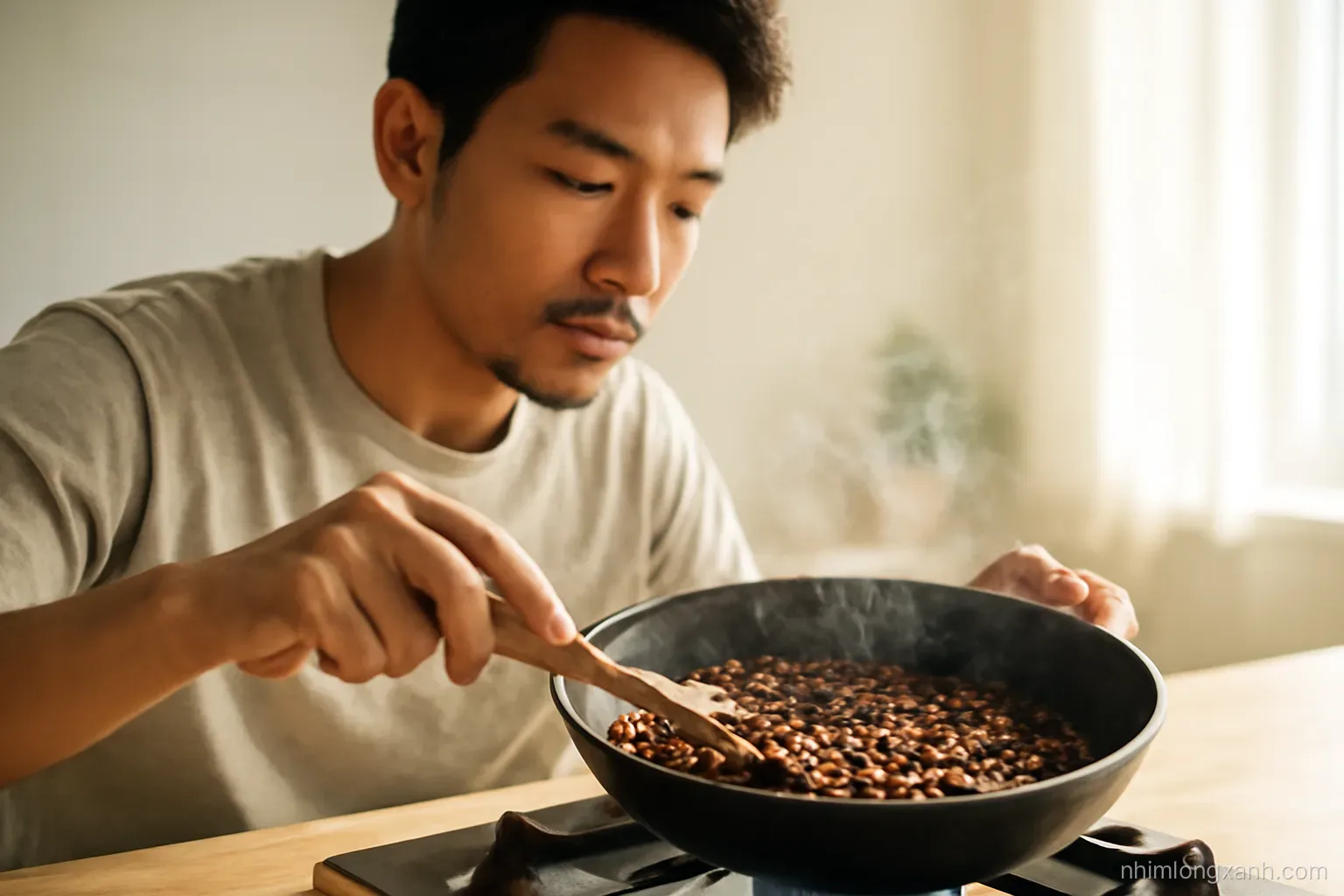 Close-up of a Vietnamese man stirring coffee beans turning from yellow to chestnut brown in a black cast iron pan on a gas stove, wisps of smoke, warm golden side light