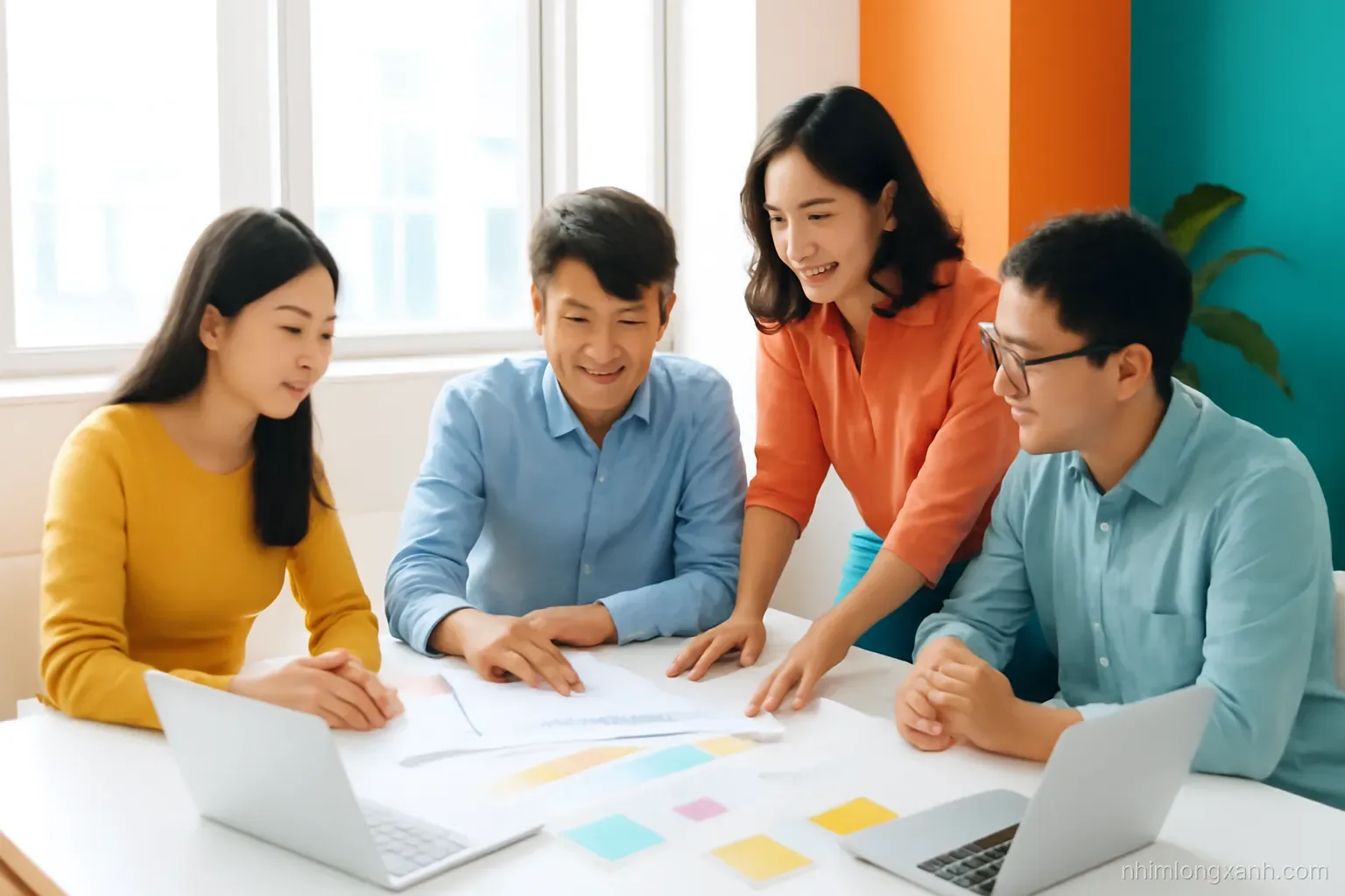 Wide shot of a small Vietnamese team reviewing figures together around a bright table, two laptops with blank glowing screens, sticky notes, sunlit modern office, orange and turquoise accents