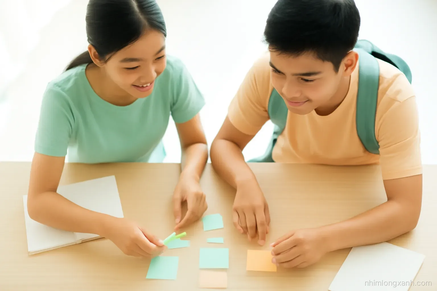 Top-down view of two Vietnamese university students at a light wooden table arranging blank pastel sticky notes and string into a branching diagram, bright natural light, mint and peach palette