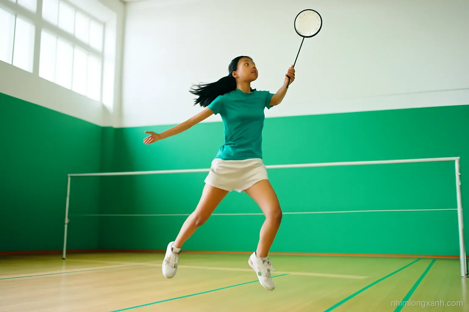 Low angle action shot of a Vietnamese teenage girl leaping for a smash in a bright indoor badminton hall, shuttlecock mid-air, wooden floor, vivid green and white tones