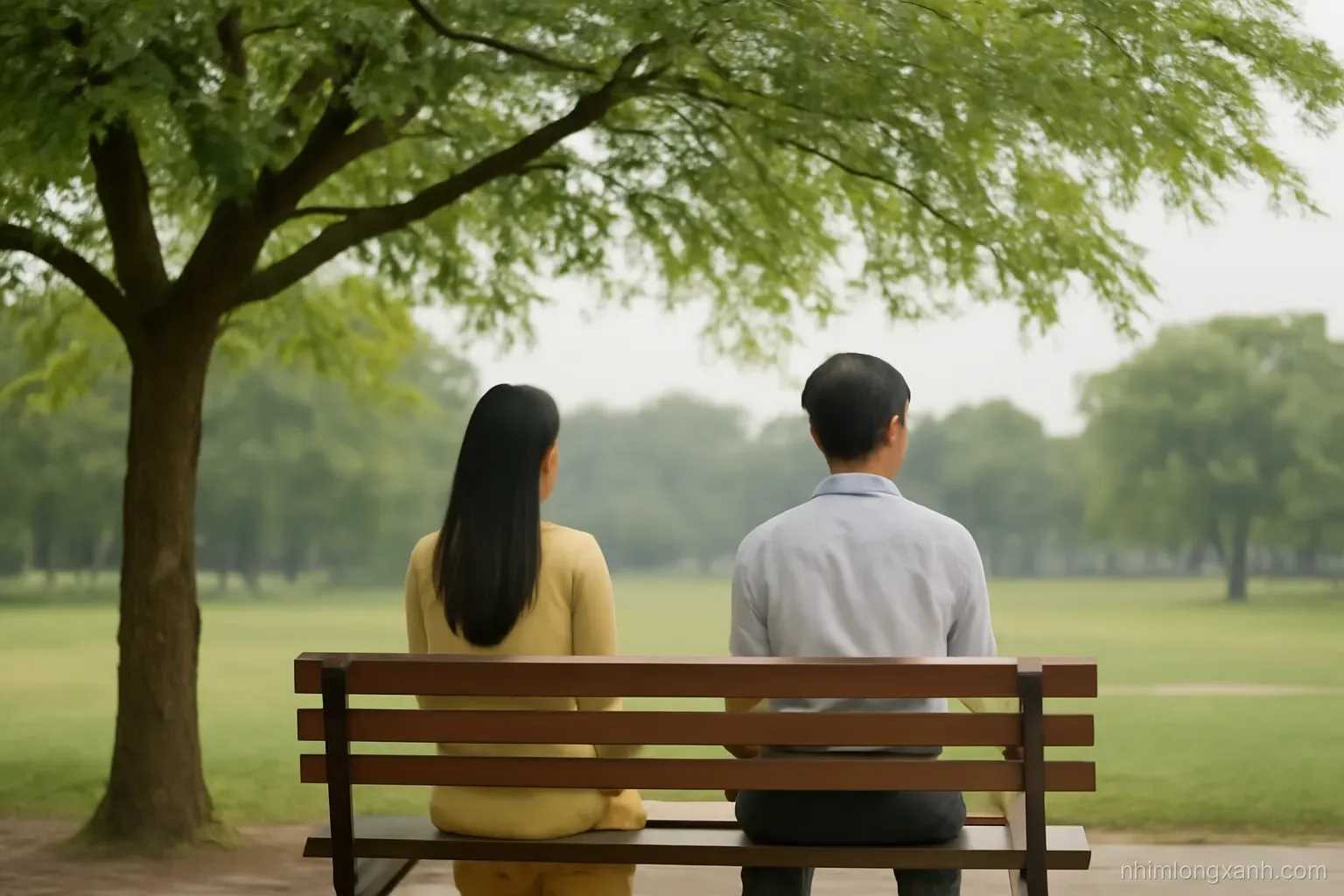 Two Vietnamese adults sitting apart on a park bench under a tamarind tree, seen from behind, wide shot, overcast soft light, muted olive and grey palette