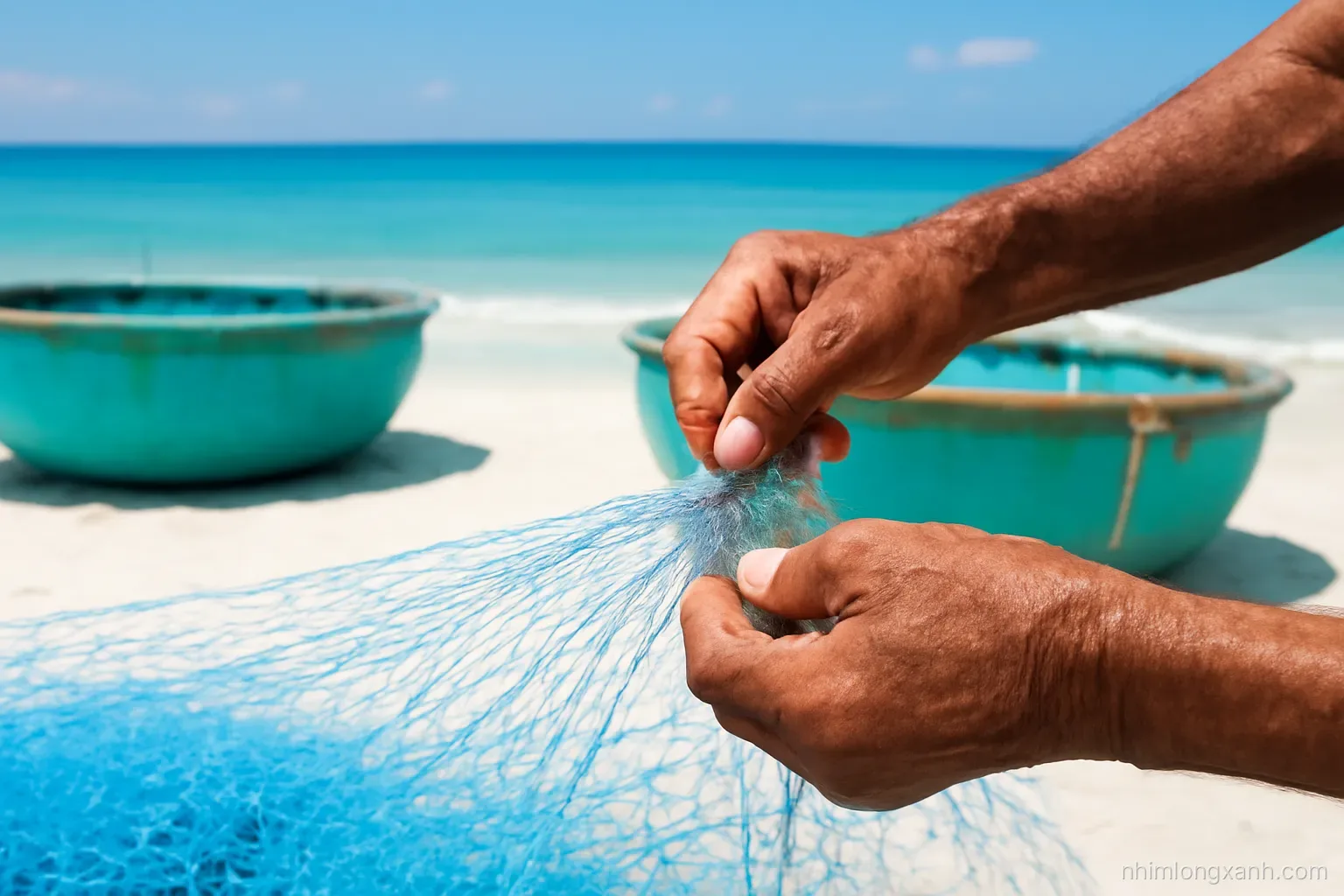Close-up of weathered Vietnamese fisherman hands repairing a blue fishing net on white sand beside round basket boats, turquoise sea behind, bright midday sun