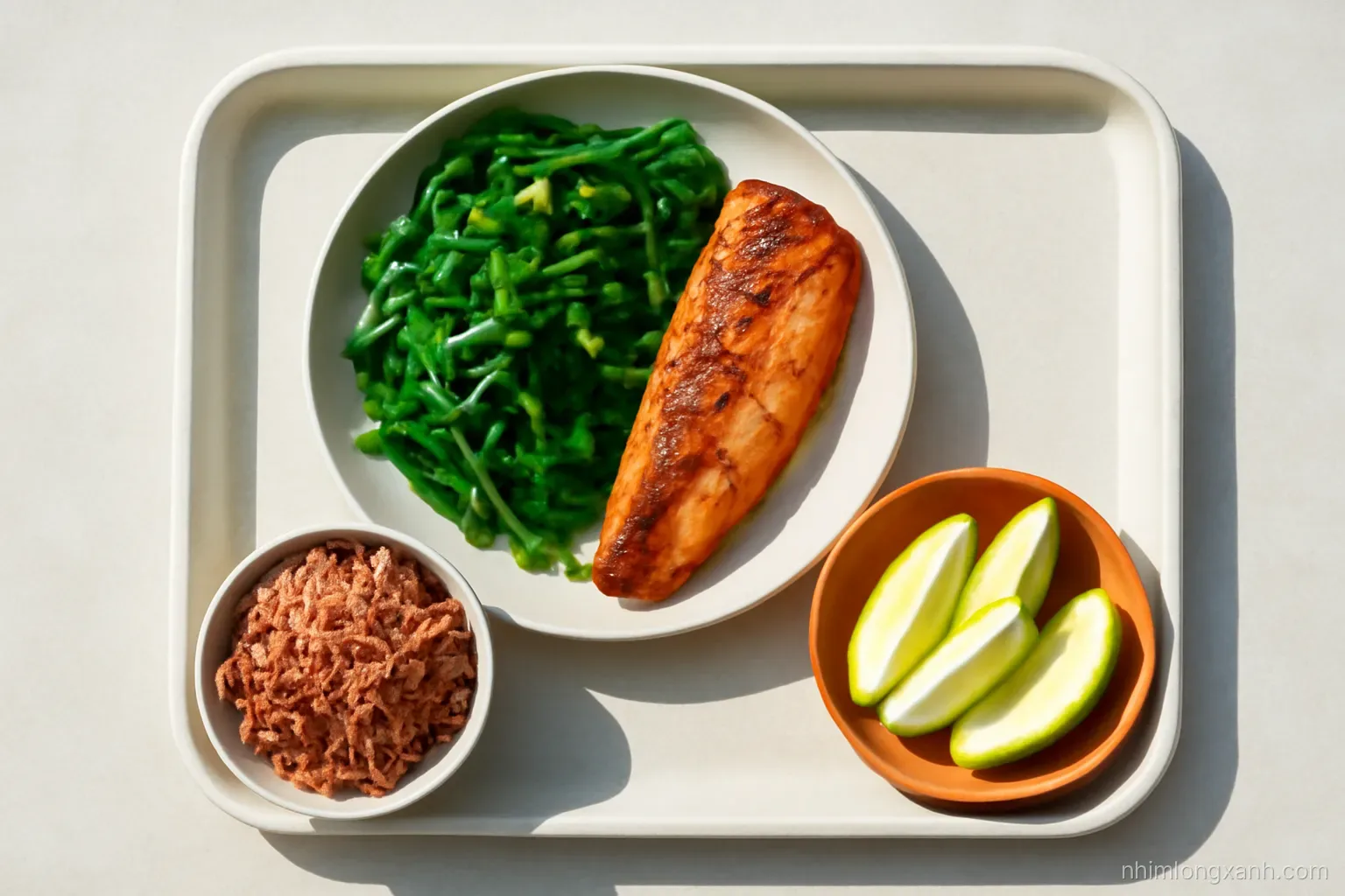 Overhead shot of a Vietnamese lunch tray with a plate half filled with stir-fried greens, grilled fish, a small bowl of brown rice, sliced guava, bright natural light, vivid green and terracotta tones