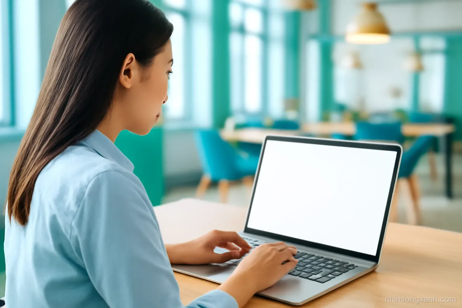 Over-the-shoulder shot of a young Vietnamese office worker pressing keys on a backlit laptop keyboard, blank glowing screen, bright airy coworking space, teal and warm yellow tones
