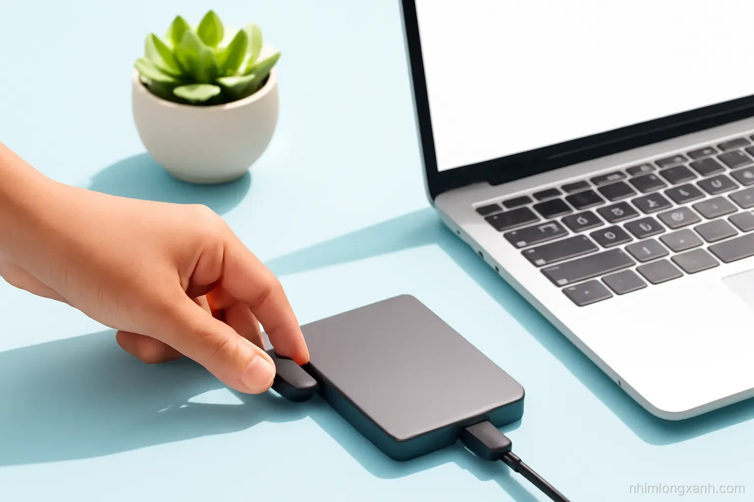 Angled 45-degree close-up of a Vietnamese hand plugging a cable into a portable external drive beside a slim laptop with blank glowing screen, sunny pastel blue desk, succulent, clean minimal style