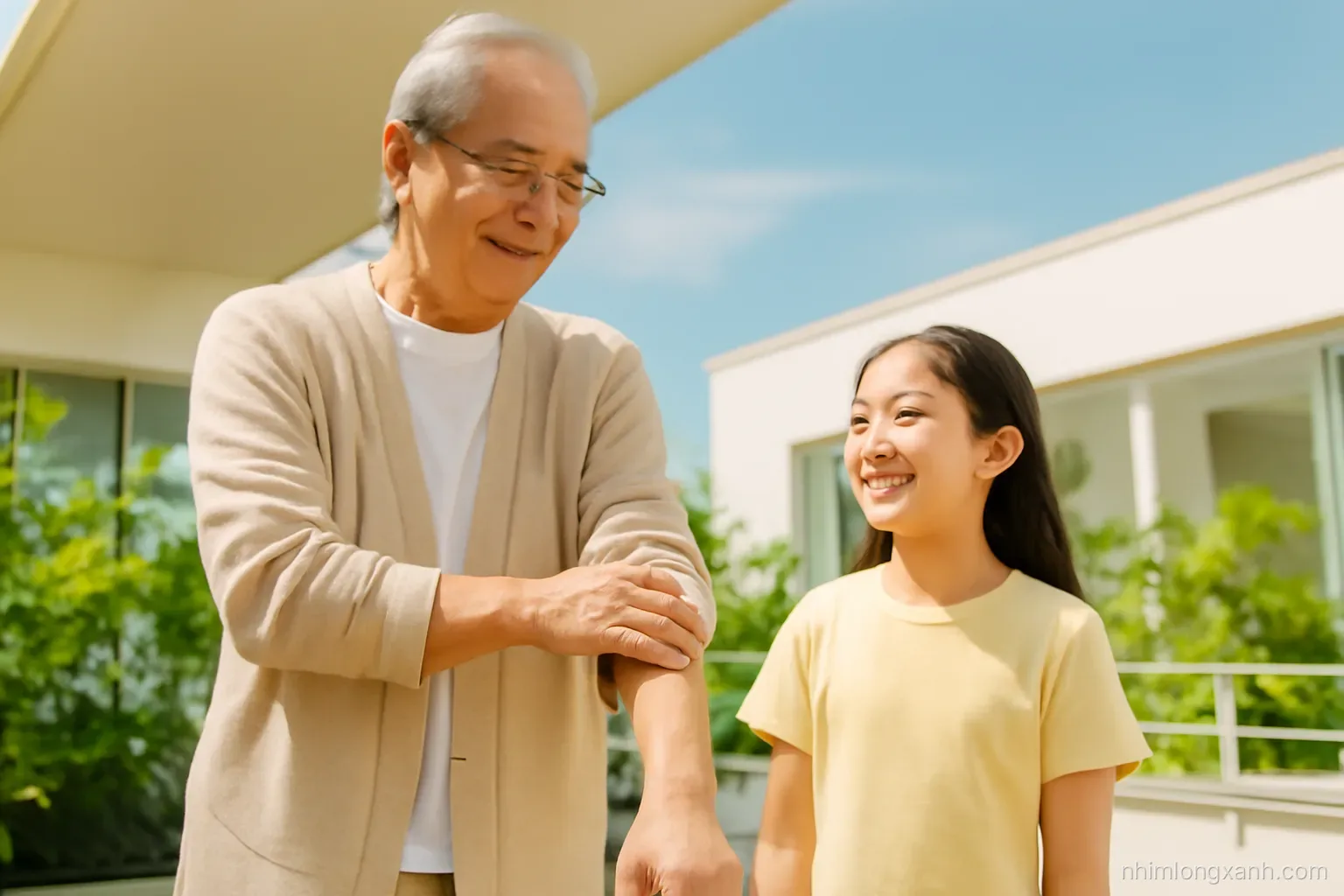 Low angle shot of a Vietnamese grandfather in a light cardigan rolling up his sleeve beside his granddaughter on a sunny clinic terrace, fresh greenery, warm golden and leaf green palette