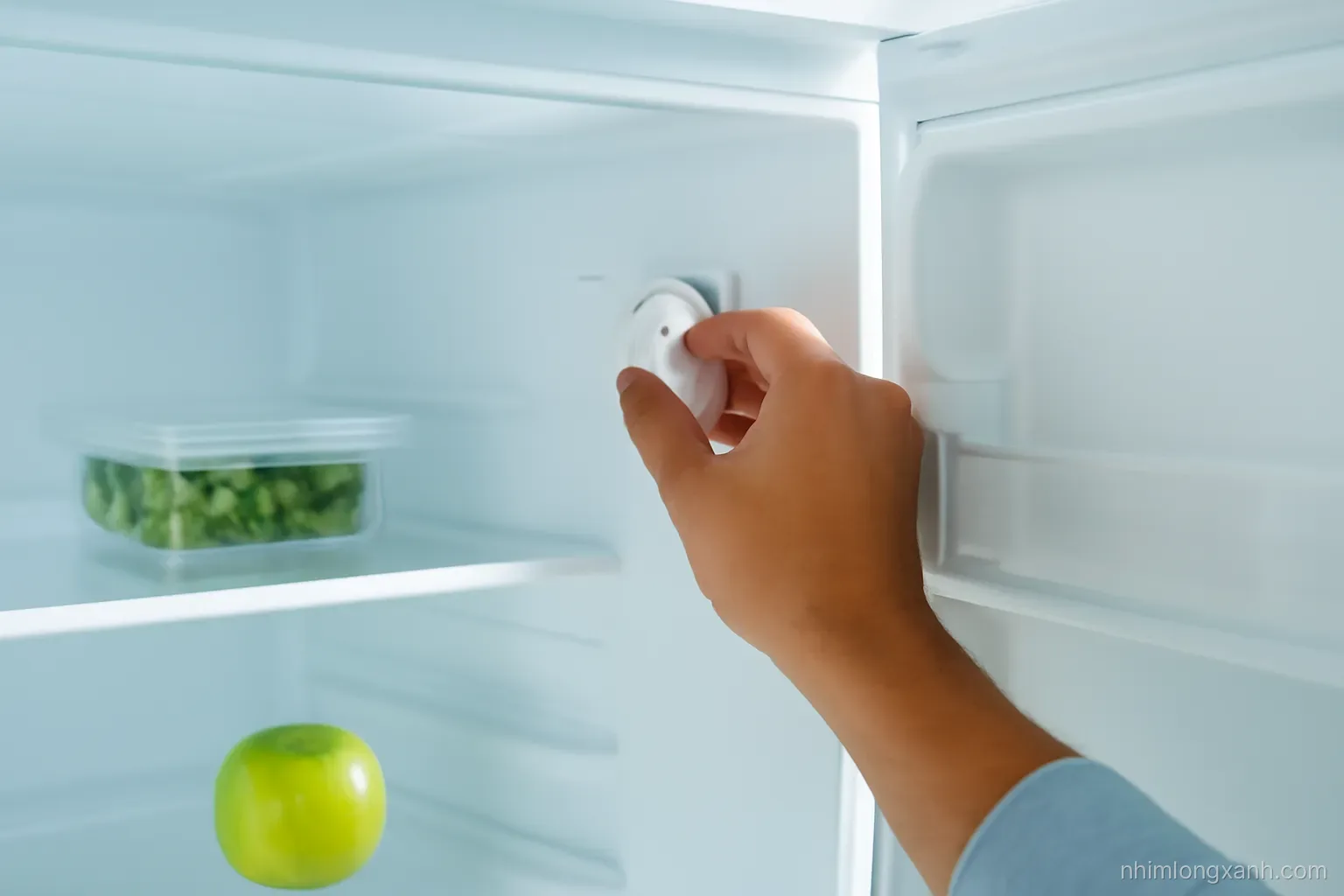 Close-up of a Vietnamese man’s hand adjusting the dial inside a clean open refrigerator, soft morning light, crisp white and pale blue palette, shallow depth of field