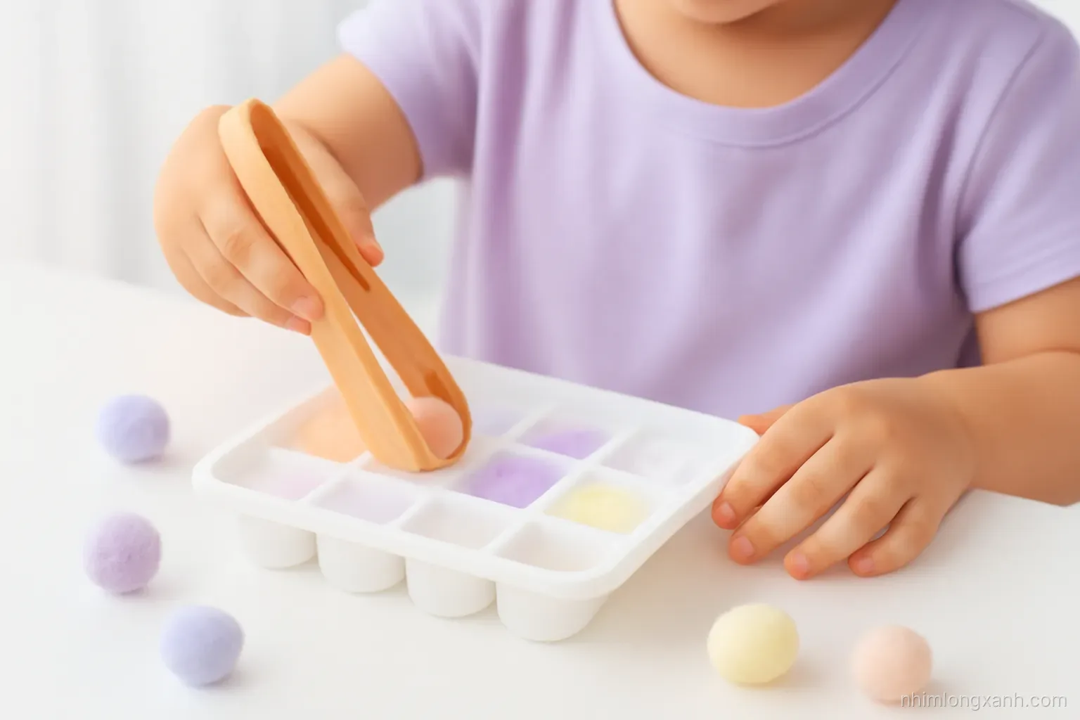 Extreme close-up of small Vietnamese child hands using wooden tongs to move pastel pom-poms into an ice cube tray, white table, soft diffused daylight, lavender and peach palette
