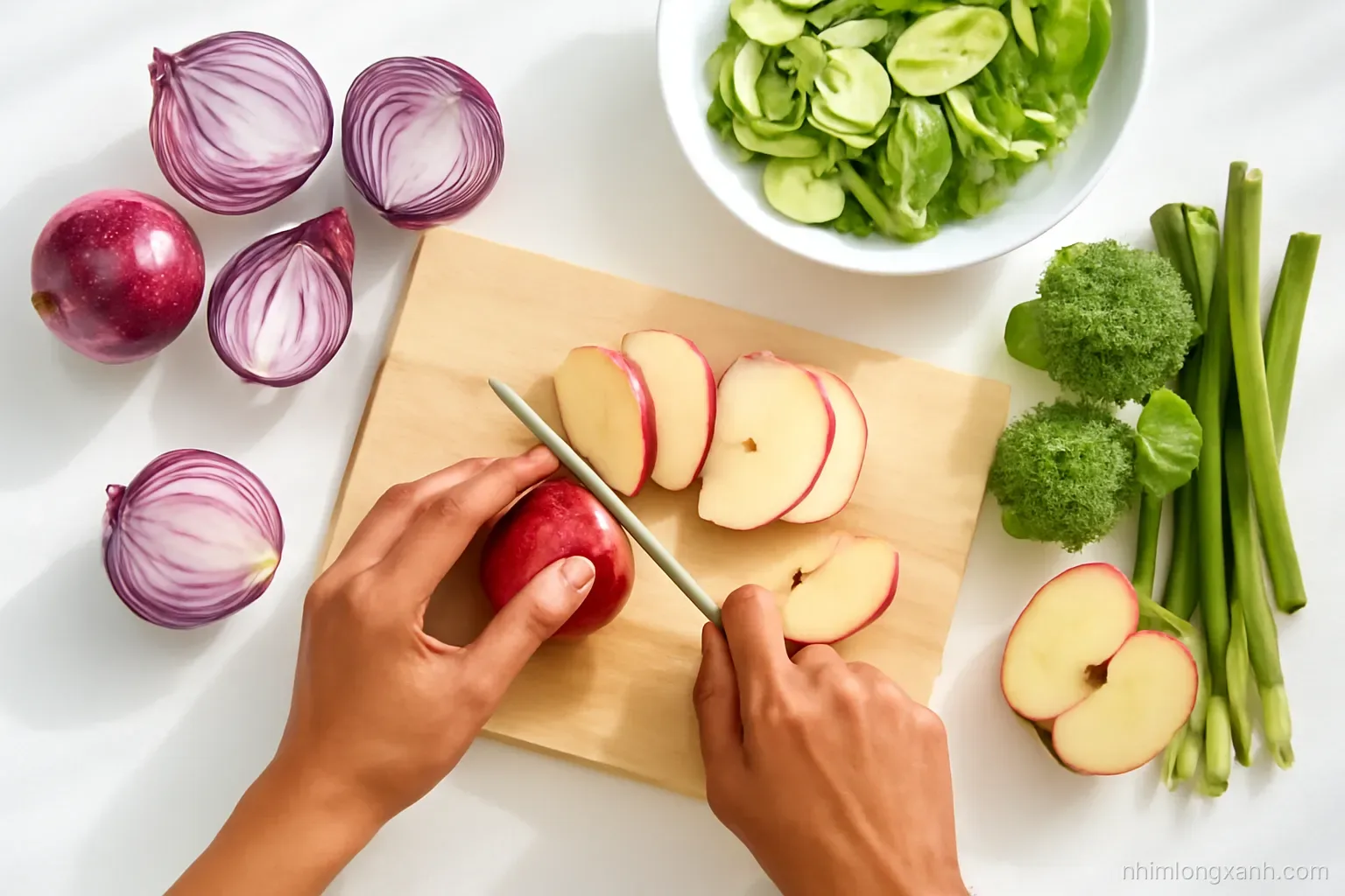 Top-down flat lay of a bright kitchen counter with halved red onions, sliced apples, green vegetables and a sharp knife on a pale wooden board, Vietnamese hands chopping, fresh daylight