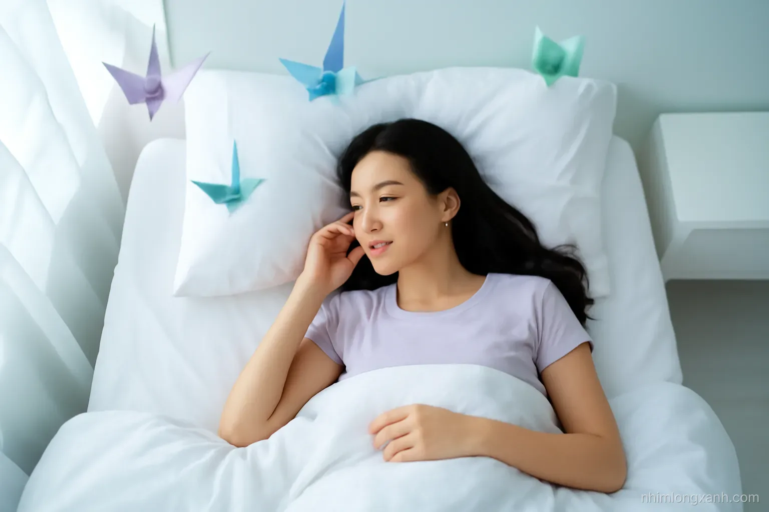 Dreamy overhead shot of a Vietnamese young woman sleeping peacefully in a white bed, soft pastel lavender and mint light, floating paper cranes above, minimalist bedroom